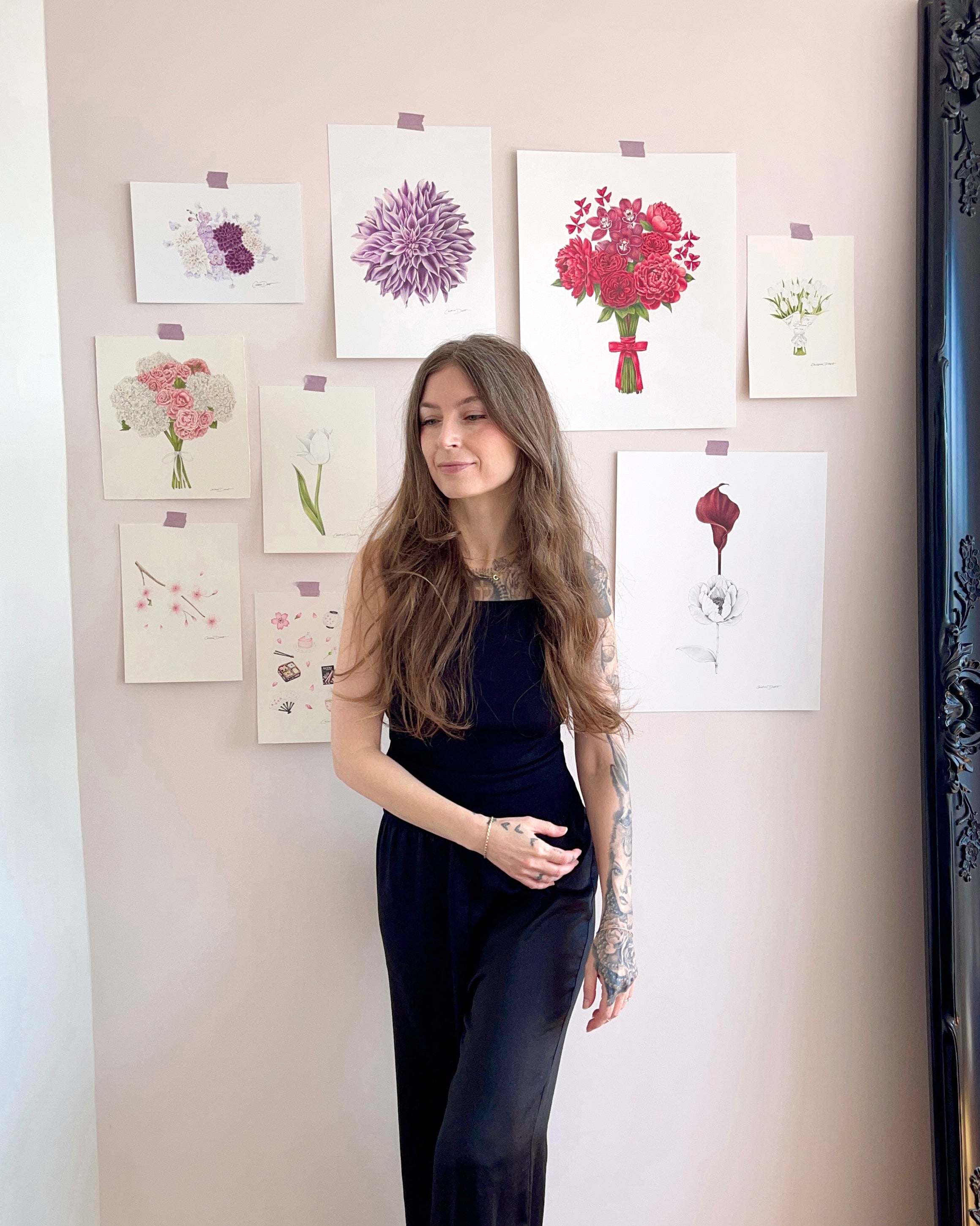 The artist in front of her floral art displayed on a light pink wall.