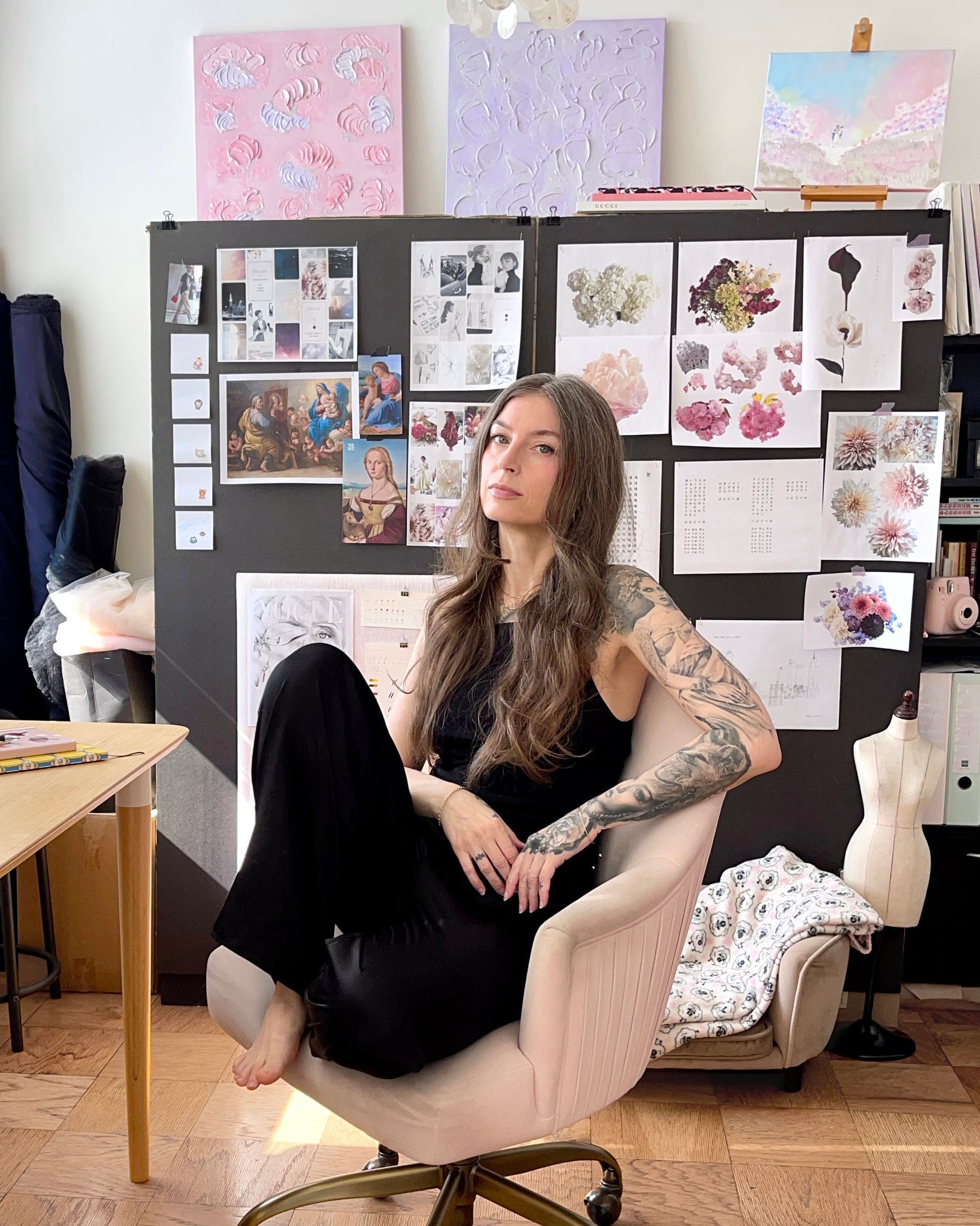 The artist sitting in her studio surrounded by art and mood boards.