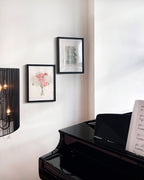 Black grand piano with sheet music against a wall with framed pictures.