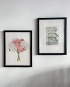 Two framed artworks on a white wall, one with flowers and the other with architectural design.