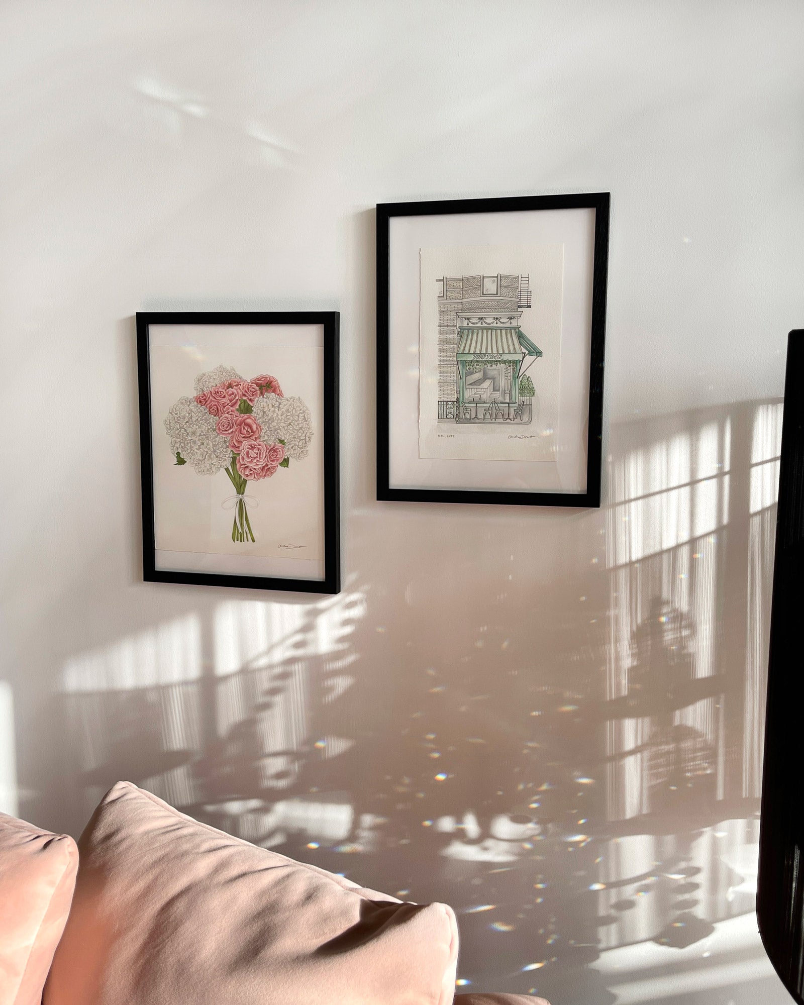 Two framed artworks on a wall with sunlight casting shadows